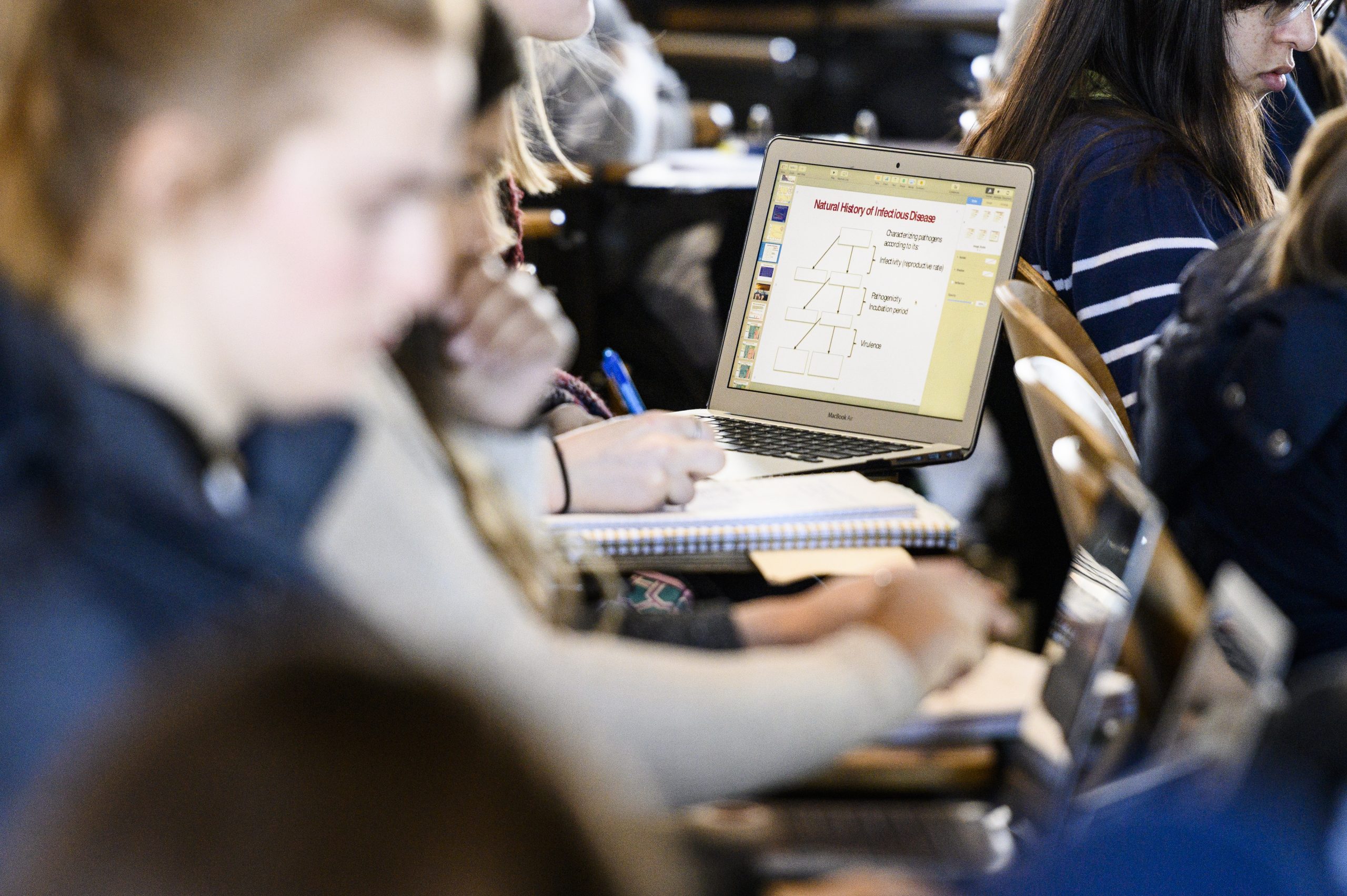 Photo focused on a student's laptop displaying slides from a lecture about infectious disease as students attend a class.